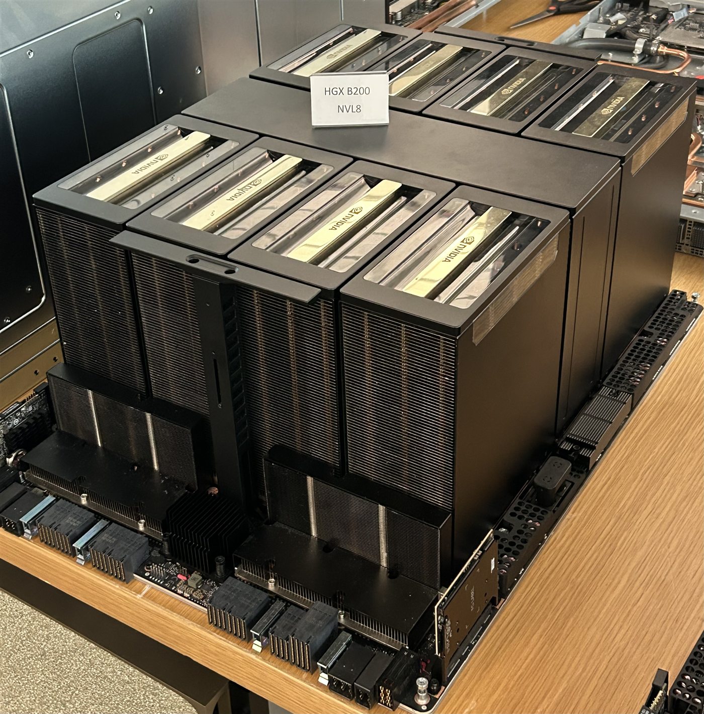 An NVIDIA HGX B200 baseboard with eight GPU heatsink towers, displayed on a table.